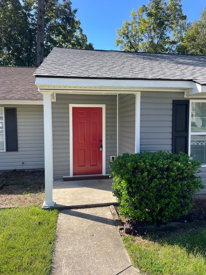 Covered front porch of a gray home with a red front door.