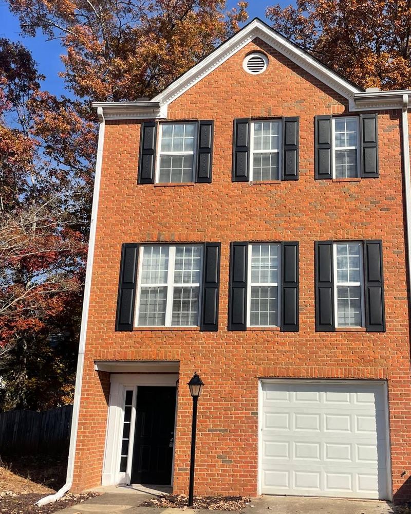 Three-story brick townhome with black shutters and a one-car garage, framed by autumn trees.