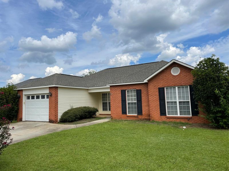 Single-story home in red brick and cream siding with black shutters and a one-car garage, under a cloudy sky.